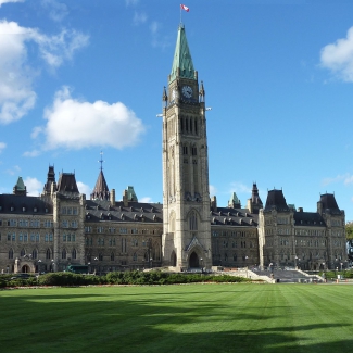Photo couleur du parlement canadien a Ottawa avec la pelouse en avant-plan et un ciel bleu avec quelques nuages.